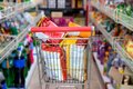 Fotografía de un carrito de supermercado lleno de enormes bolsas de patatas fritas, en medio de dos pasillos de supermercado con más productos ultraprocesados.